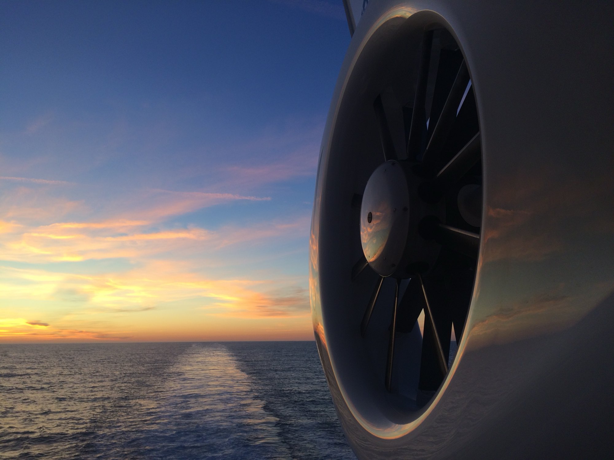 A ship's funnel against a sunset, with the vessel's wake trailing to the horizon.