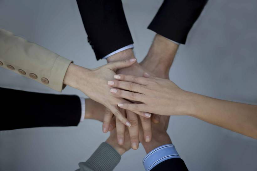 Colleagues joining hands over a table.